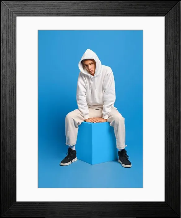 Framed Print : Young man in white sweatshirt with hood and sweatpants sits on wooden cube over blue studio background Framed Print : Young man in white sweatshirt with hood and sweatpants sits on wooden cube over blue studio background