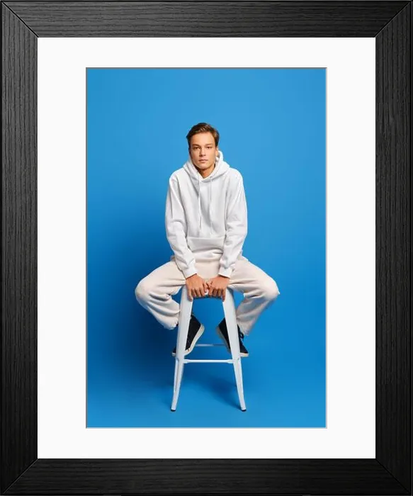 Framed Print : Handsome man wearing white sweatshirt and sweatpants sitting on white chair over blue studio background Framed Print : Handsome man wearing white sweatshirt and sweatpants sitting on white chair over blue studio background