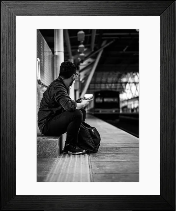Framed Print : A vertical shot of a man waiting for his train in black and white Framed Print : A vertical shot of a man waiting for his train in black and white