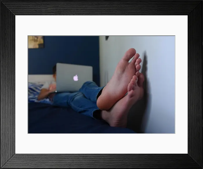 Framed Print : A teenage boy (AGE 14) lays on his bed with a mac book air laptop doing his homework fully clothed but with bare feet Framed Print : A teenage boy (AGE 14) lays on his bed with a mac book air laptop doing his homework fully clothed but with bare feet