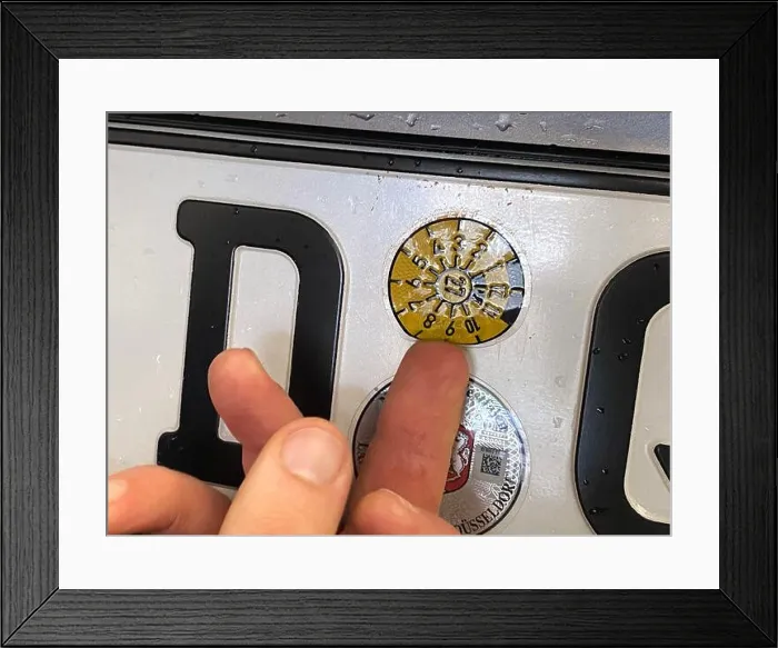 Framed Print : Eine frische TÜV-Plakette wird von dem Prüfer auf ein Autokennzeichen geklebt Framed Print : Eine frische TÜV-Plakette wird von dem Prüfer auf ein Autokennzeichen geklebt