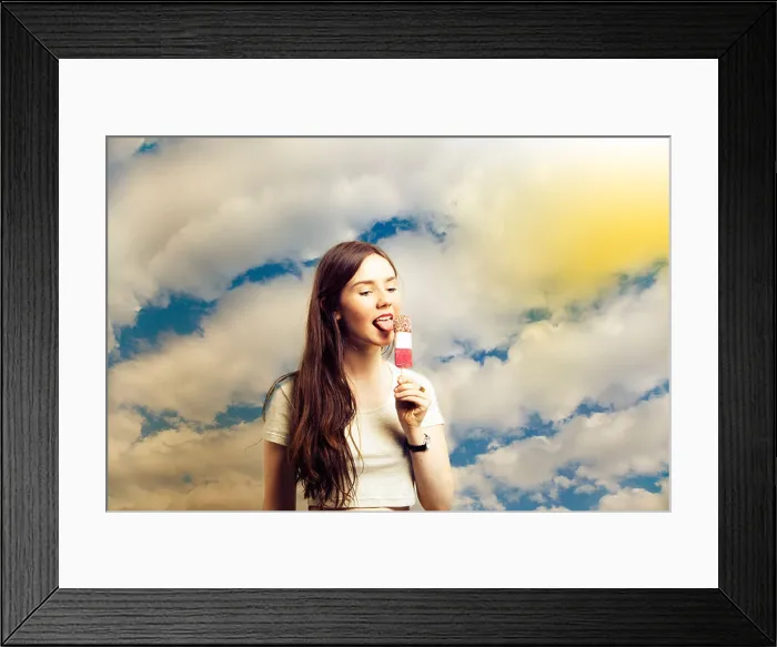 Framed Print : Beautiful young woman licking popsicle against cloudy sky