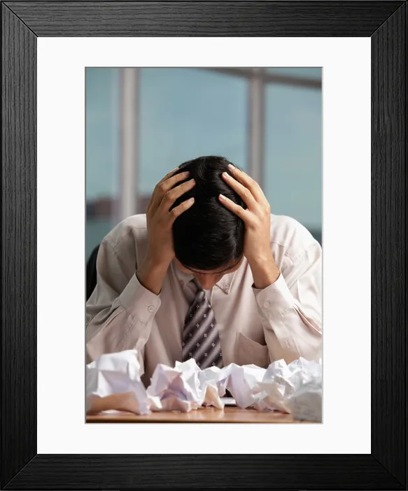 Framed Print : Indian man holding head with crumpled up paper on table Framed Print : Indian man holding head with crumpled up paper on table