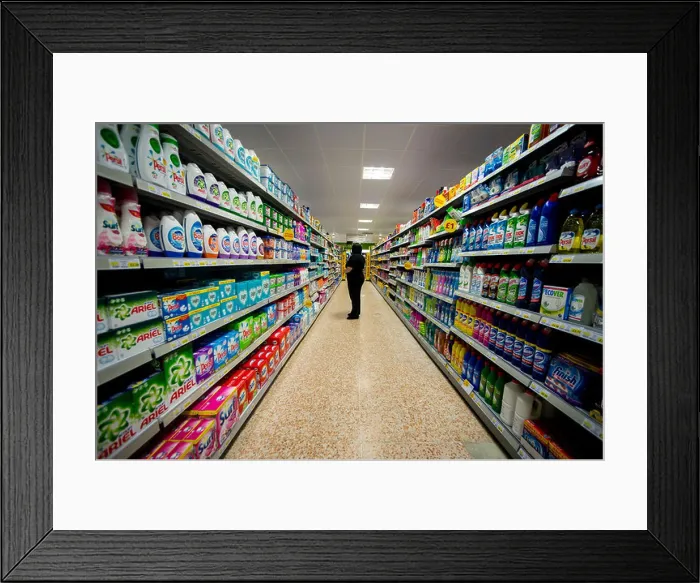 Framed Print : Fully stocked isle in a supermarket. A staff member observes the shelves for possible re stocking Framed Print : Fully stocked isle in a supermarket. A staff member observes the shelves for possible re stocking