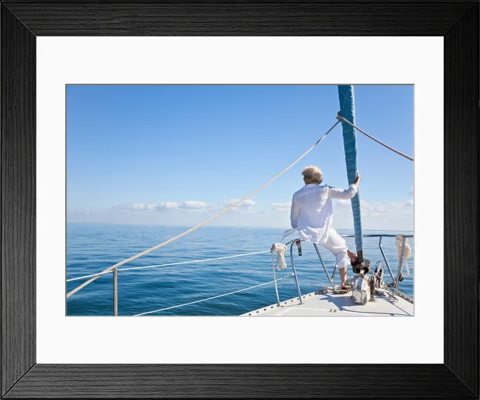 Framed Print : Rear view of a senior woman alone sitting on the front of a sail boat on a calm blue sea Framed Print : Rear view of a senior woman alone sitting on the front of a sail boat on a calm blue sea