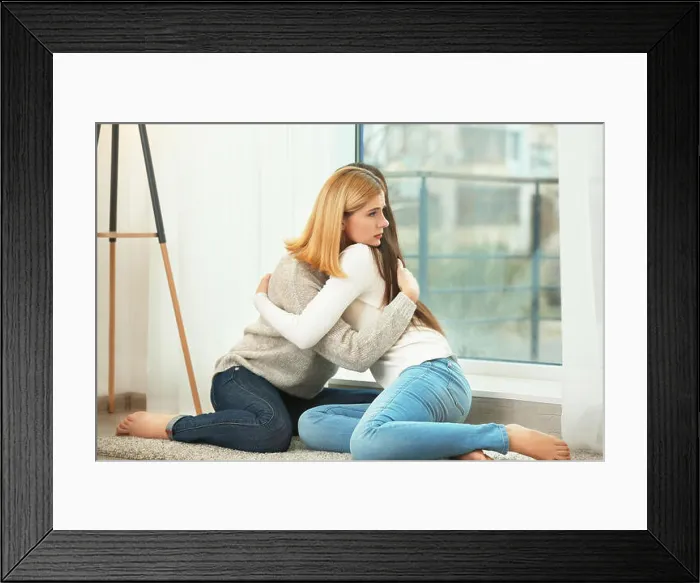 Framed Print : Beautiful woman hugging depressed friend while sitting on floor at home Framed Print : Beautiful woman hugging depressed friend while sitting on floor at home