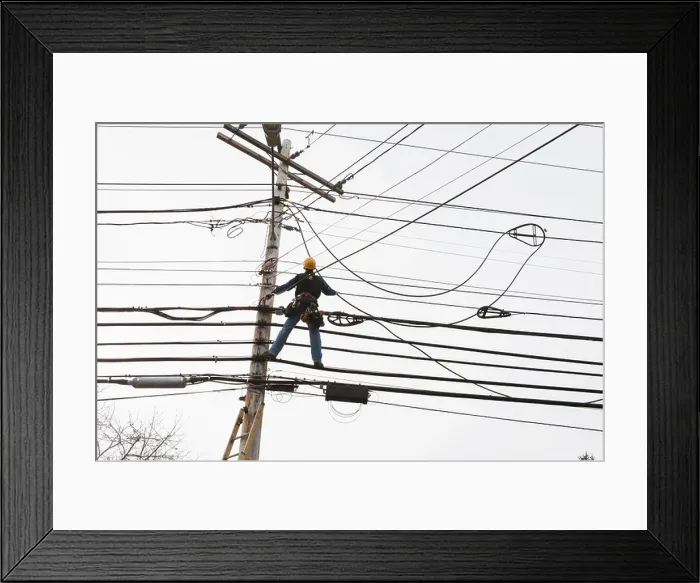 Framed Print : Communications worker on a power pole installing new cable to existing bundles Framed Print : Communications worker on a power pole installing new cable to existing bundles