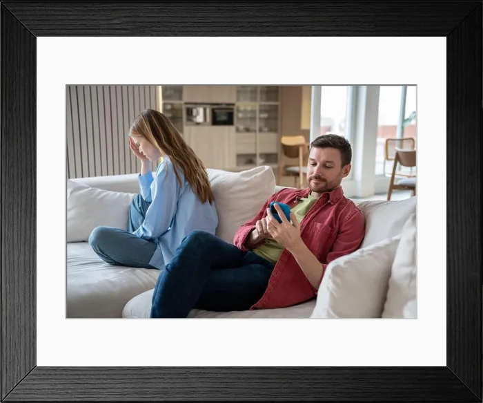 Framed Print : Husband ignoring wife emotions looking at smartphone screen sitting on couch at home Framed Print : Husband ignoring wife emotions looking at smartphone screen sitting on couch at home