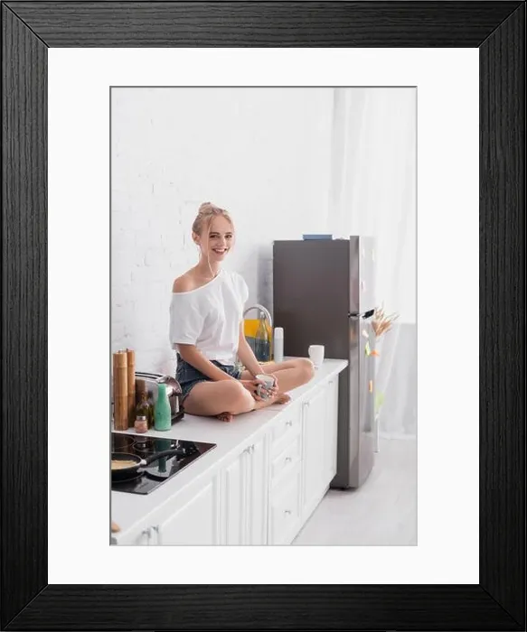 Framed Print : joyful woman sitting on kitchen table with crossed legs and looking at camera Framed Print : joyful woman sitting on kitchen table with crossed legs and looking at camera