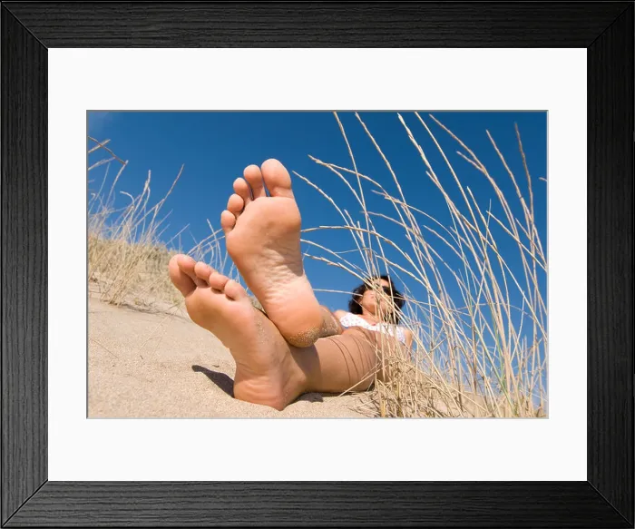 Framed Print : Model Released female feet lying in sand dunes with blue sky and focus on feet Framed Print : Model Released female feet lying in sand dunes with blue sky and focus on feet