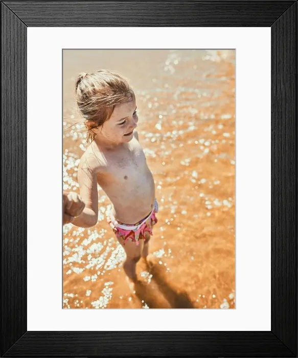 Framed Print : Close up of happy little girl standing in the sea looking away holding parent's hand Framed Print : Close up of happy little girl standing in the sea looking away holding parent's hand