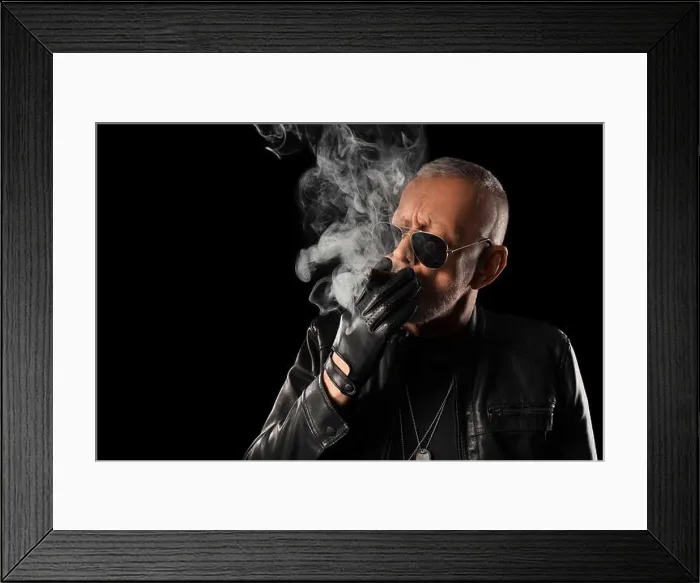 Framed Print : Stylish old man in leather jacket smoking cigar on black background
