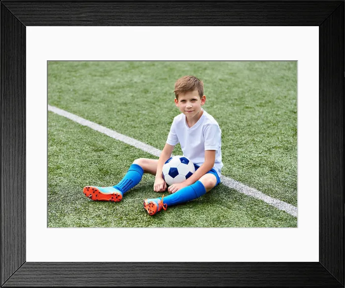 Framed Print : Boy football soccer with ball sitting on a green grass Framed Print : Boy football soccer with ball sitting on a green grass