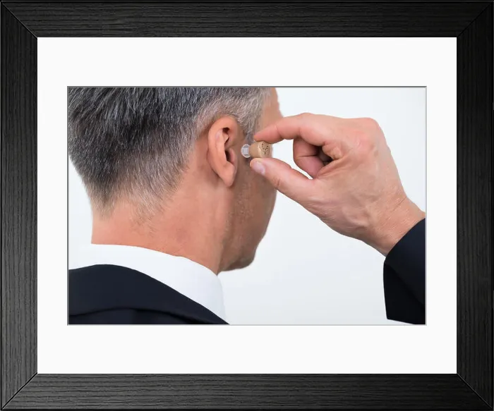 Framed Print : Rear view of businessman inserting hearing aid in ear over white background Framed Print : Rear view of businessman inserting hearing aid in ear over white background