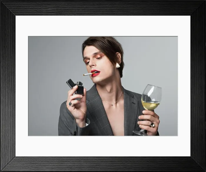 Framed Print : young transgender man in blazer holding glass of wine and lighter while smoking isolated on grey Framed Print : young transgender man in blazer holding glass of wine and lighter while smoking isolated on grey