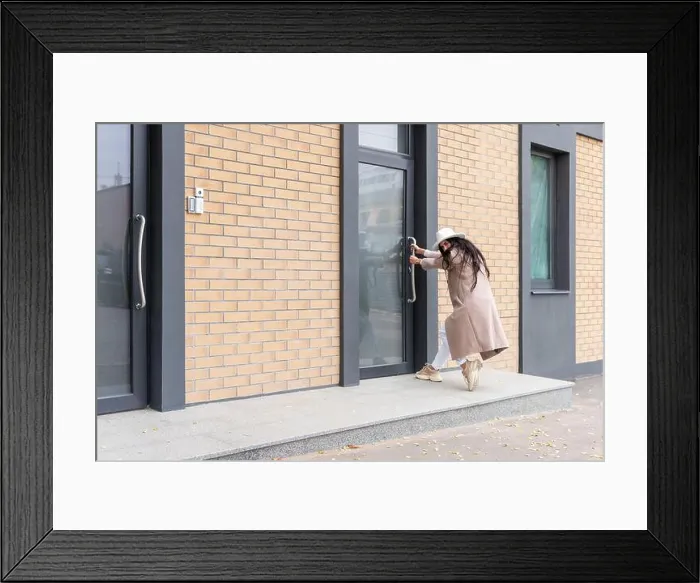 Framed Print : woman in a coat and hat tries to open a closed door, pulls the door by the handle Framed Print : woman in a coat and hat tries to open a closed door, pulls the door by the handle