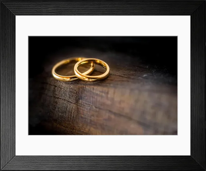 Framed Print : Close up of two golden wedding rings lying on the edge of an ancient and weathered wooden table Framed Print : Close up of two golden wedding rings lying on the edge of an ancient and weathered wooden table