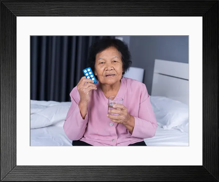 Framed Print : senior woman taking pill with glass of water in a bed