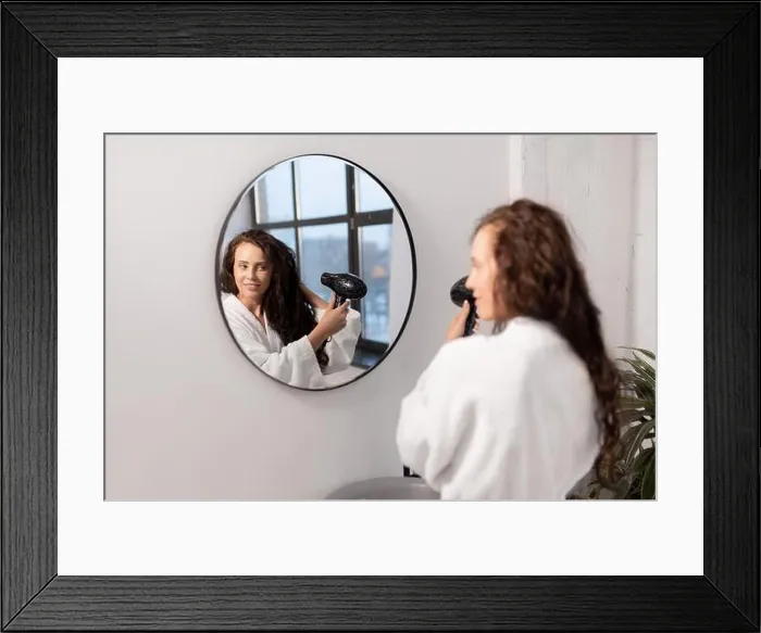 Framed Print : Charming young female with hair-dryer taking care of her dark long wavy hair Framed Print : Charming young female with hair-dryer taking care of her dark long wavy hair