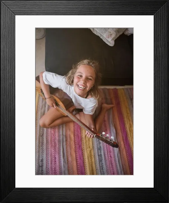 Framed Print : From above of happy preteen girl in casual clothes smiling broadly and looking at camera while sitting on carpet Framed Print : From above of happy preteen girl in casual clothes smiling broadly and looking at camera while sitting on carpet