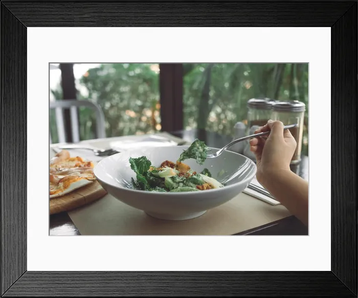 Framed Print : A hand using fork to scoop up Ceasar salad to eat with pizza on dining table in the restaurant Framed Print : A hand using fork to scoop up Ceasar salad to eat with pizza on dining table in the restaurant