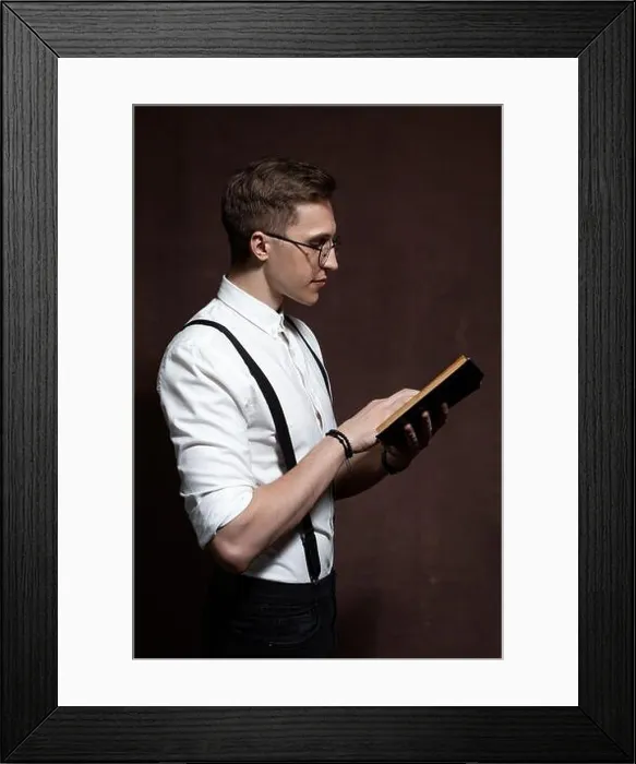 Framed Print : elegant young man in round glasses, suspenders, in a white shirt reads a book Framed Print : elegant young man in round glasses, suspenders, in a white shirt reads a book