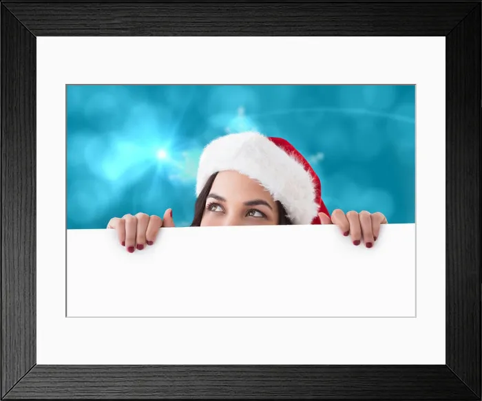 Framed Print : Pretty brunette in santa hat showing white poster against blurred christmas background Framed Print : Pretty brunette in santa hat showing white poster against blurred christmas background