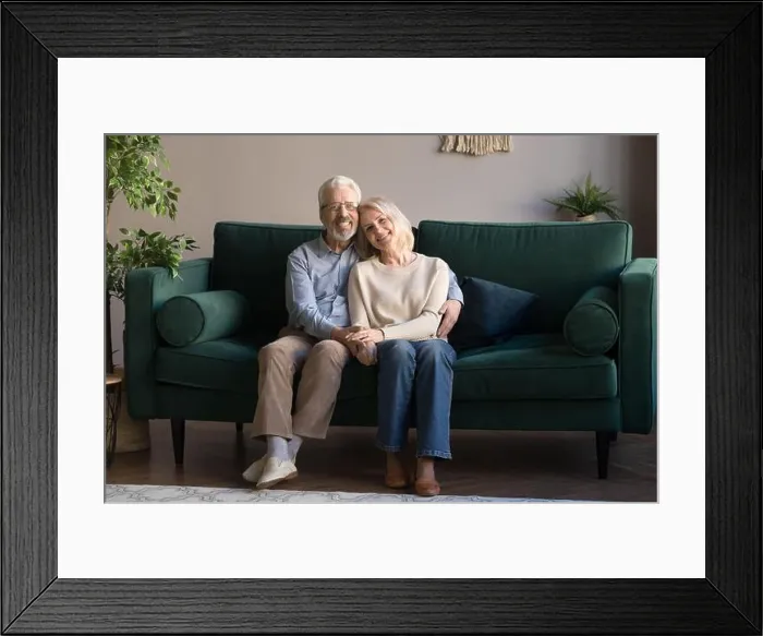 Framed Print : Mature couple embracing sitting on couch posing for camera Framed Print : Mature couple embracing sitting on couch posing for camera