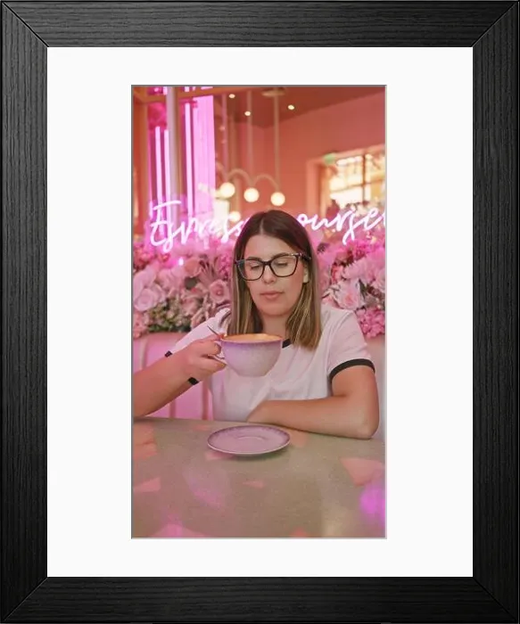 Framed Print : Adult hispanic woman enjoying coffee in a pink-themed cafe with neon lights and floral decorations Framed Print : Adult hispanic woman enjoying coffee in a pink-themed cafe with neon lights and floral decorations