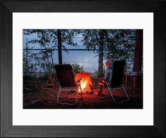 Framed Print : Woman sitting by the campfire in the forest on the banks of Lake Siljan in Dalarna, Sweden
