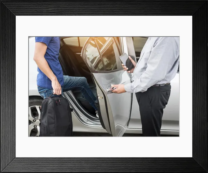Framed Print : Taxi driver greeting his passengers with their luggage on the sidewalk of a modern city Framed Print : Taxi driver greeting his passengers with their luggage on the sidewalk of a modern city