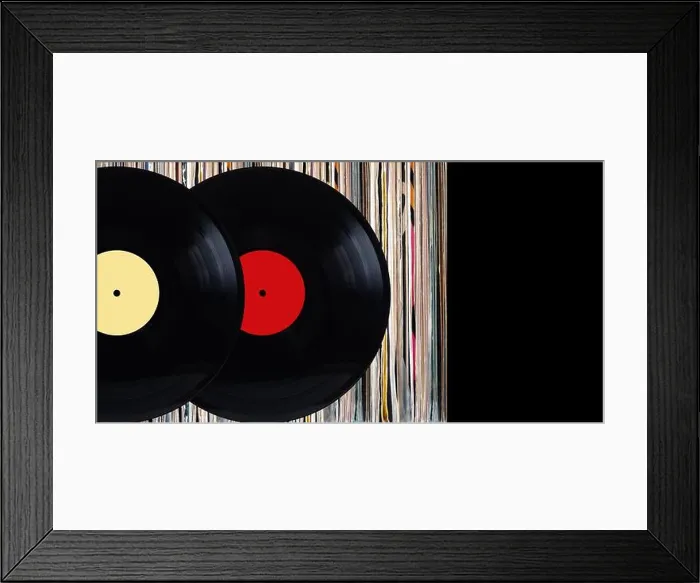 Framed Print : Two black vinyl records with color labels in front of shelf of many close standing vinyl discs in old color covers over Framed Print : Two black vinyl records with color labels in front of shelf of many close standing vinyl discs in old color covers over