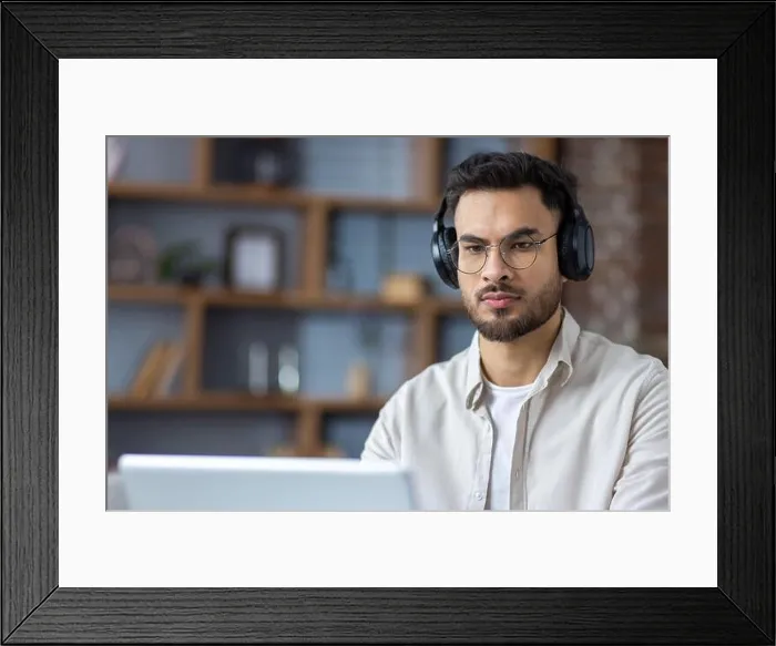 Framed Print : Close-up photo of a serious and focused young Indian man wearing headphones working and studying on a laptop at home Framed Print : Close-up photo of a serious and focused young Indian man wearing headphones working and studying on a laptop at home