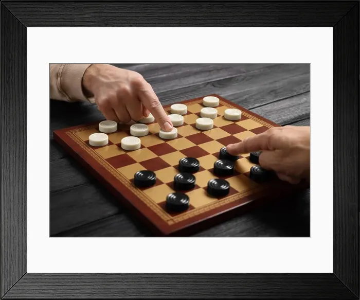 Framed Print : Man playing checkers with partner at black wooden table, closeup