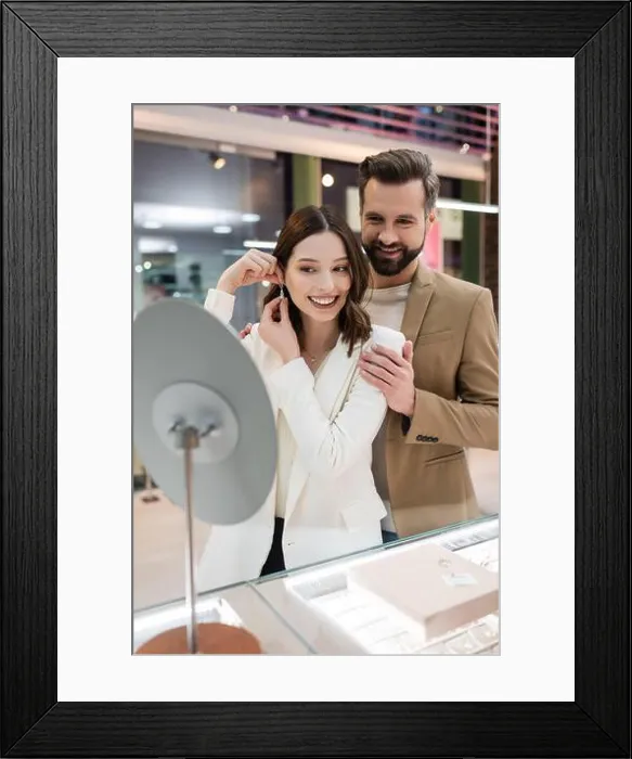Framed Print : Cheerful man hugging girlfriend wearing earring near mirror in jewelry shop Framed Print : Cheerful man hugging girlfriend wearing earring near mirror in jewelry shop