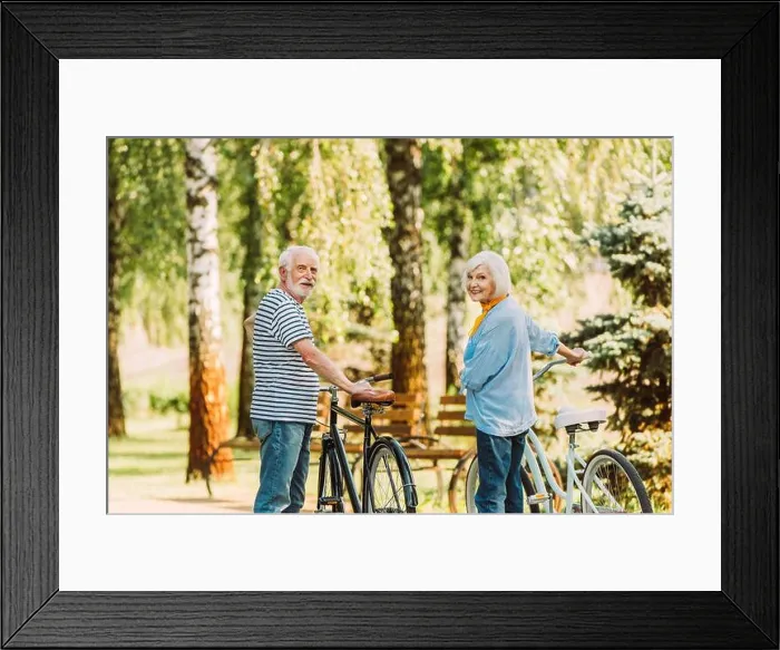 Framed Print : Senior couple smiling at camera while standing near bicycles in park Framed Print : Senior couple smiling at camera while standing near bicycles in park