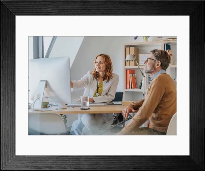 Framed Print : General practitioner using computer while sitting by patient at doctor's office
