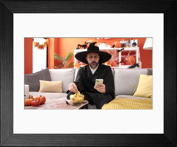 Framed Print : Young bald man wearing wizard costume eating chips potatoes using smartphone at home Framed Print : Young bald man wearing wizard costume eating chips potatoes using smartphone at home