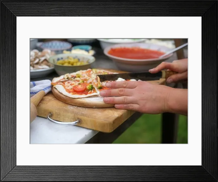 Framed Print : Hands cutting freshly baked pizza on a rustic wooden board Framed Print : Hands cutting freshly baked pizza on a rustic wooden board