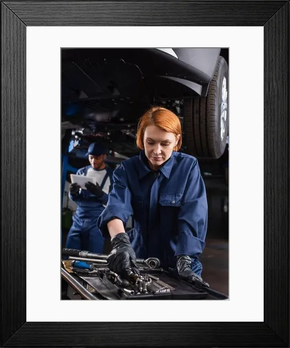 Framed Print : Mechanic in uniform taking tool near blurred african american colleague with digital tablet and car in garage Framed Print : Mechanic in uniform taking tool near blurred african american colleague with digital tablet and car in garage