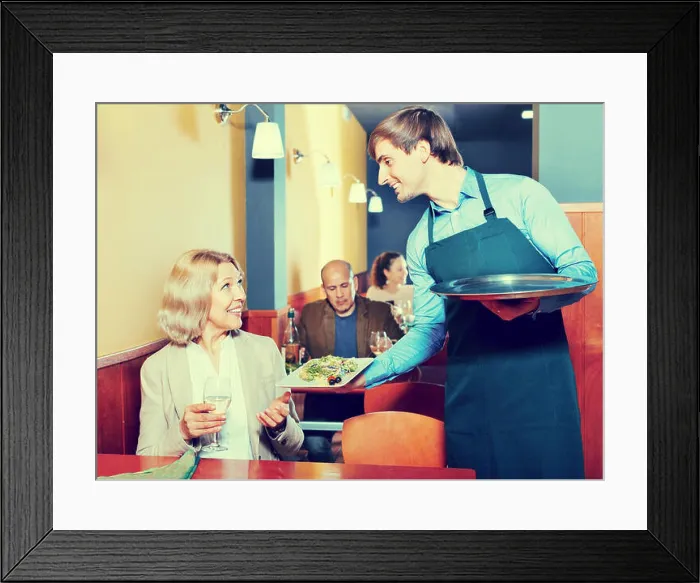 Framed Print : Positive waiter bringing order to happy smiling mature female in restaurant Framed Print : Positive waiter bringing order to happy smiling mature female in restaurant