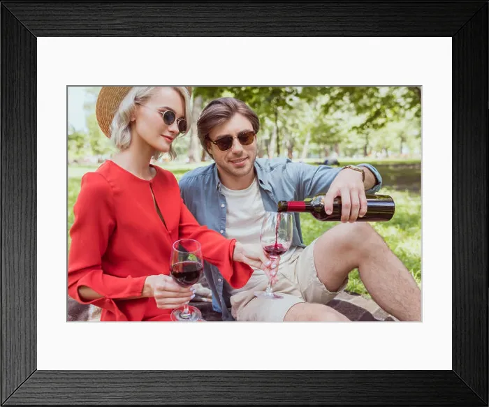 Framed Print : boyfriend pouring red wine in glasses from bottle in park