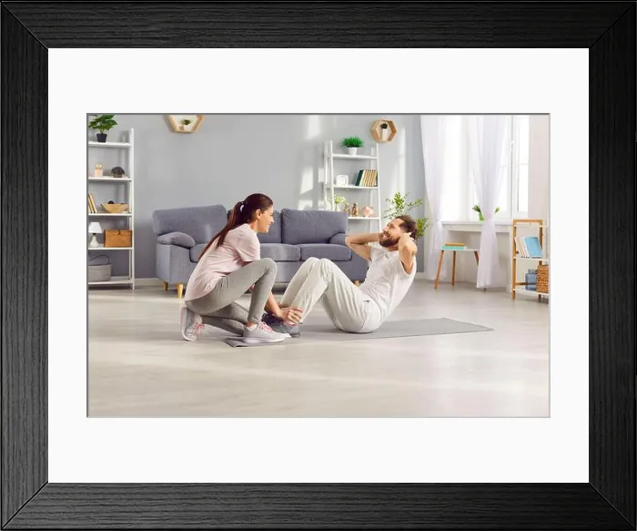 Framed Print : Happy sporty young woman helping her husband doing sport fit exercises at home Framed Print : Happy sporty young woman helping her husband doing sport fit exercises at home