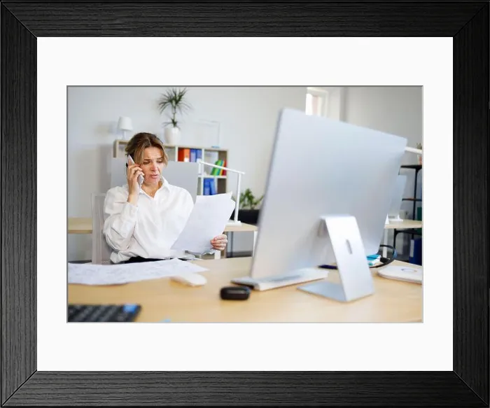 Framed Print : Woman accountant indignantly looks at documents and talks on the smartphone Framed Print : Woman accountant indignantly looks at documents and talks on the smartphone