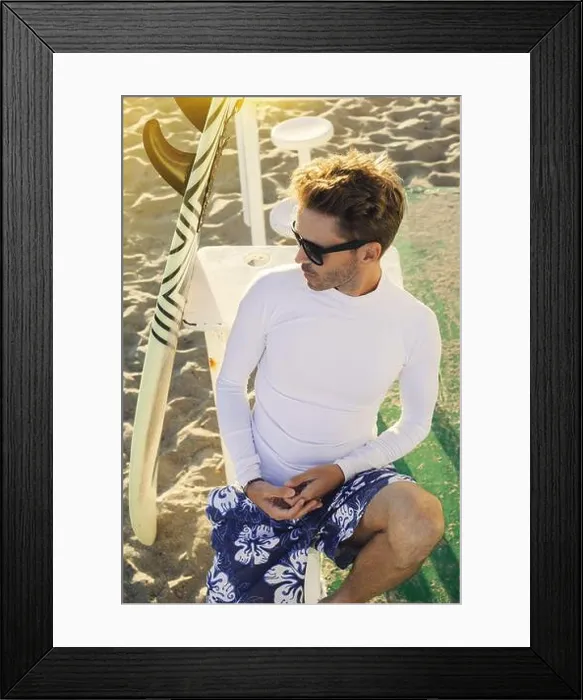 Framed Print : Young handsome smiling man is sitting on a beach next to his surfboard wearing dark sunglasses Framed Print : Young handsome smiling man is sitting on a beach next to his surfboard wearing dark sunglasses