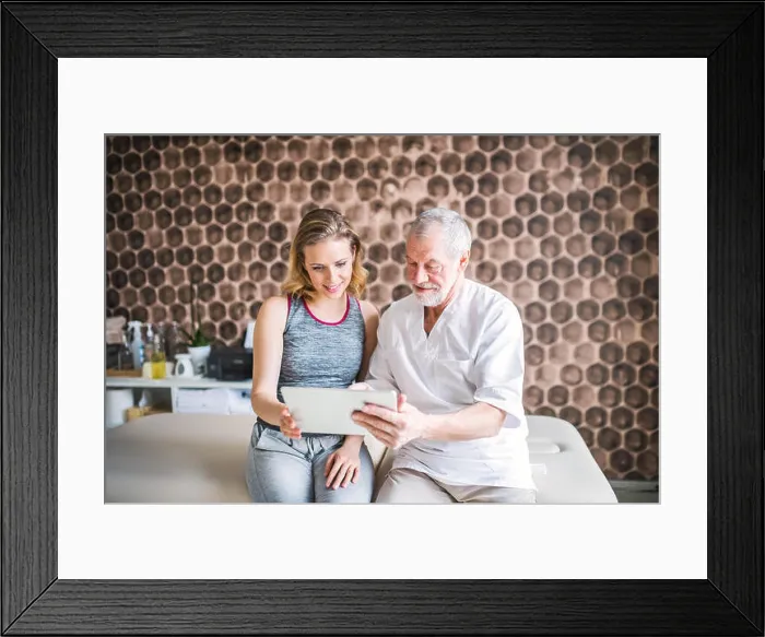 Framed Print : Senior male physiotherapist and young woman with tablet sitting Framed Print : Senior male physiotherapist and young woman with tablet sitting