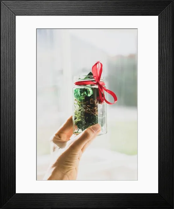 Framed Print : Hand holding Christmas decorations in a jar with ribbon in front of a window Framed Print : Hand holding Christmas decorations in a jar with ribbon in front of a window