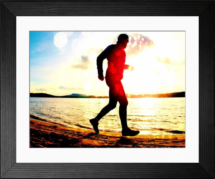 Framed Print : Film grain effect. Tall man with sunglass and dark cap is running on the beach at sunset