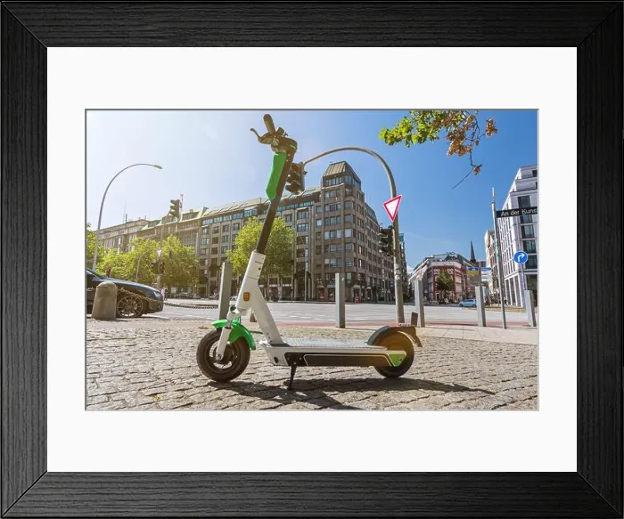 Framed Print : E-Scooter standing on the pavement in a big city with scenic lens flare Framed Print : E-Scooter standing on the pavement in a big city with scenic lens flare