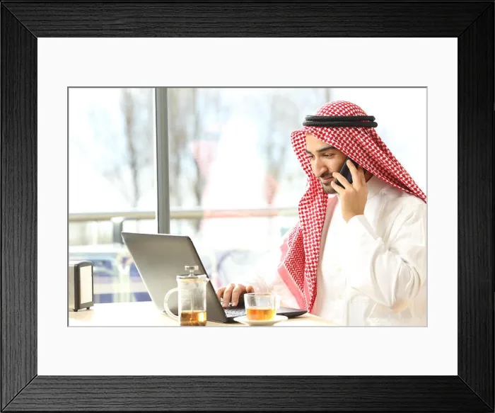 Framed Print : Arab man working on the phone and a laptop in a coffee shop with a window in the background Framed Print : Arab man working on the phone and a laptop in a coffee shop with a window in the background
